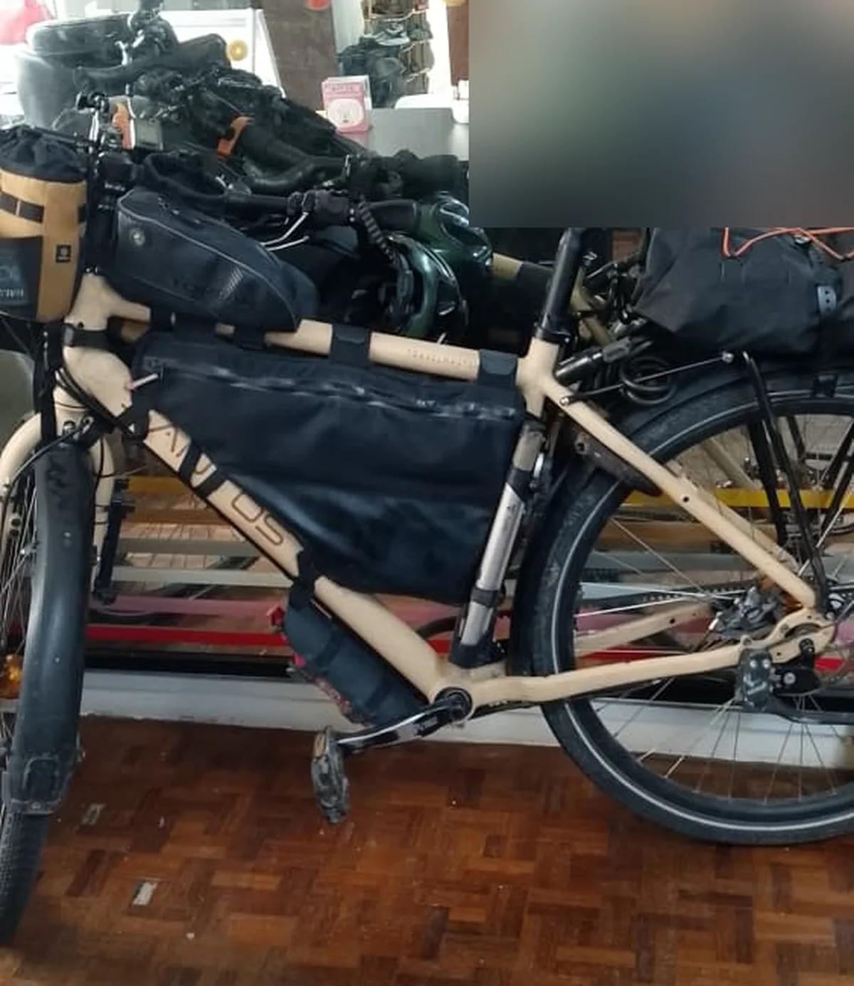 A loaded bikepacking touring bicycle with frame bag and handlebar bag parked inside the reception area of Pelangi Capsule Hostel in Johor Bahru