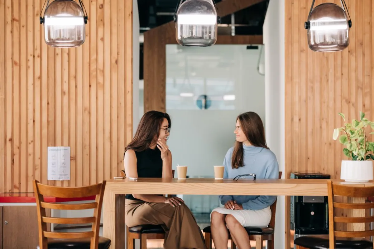 Two friends from different backgrounds chatting over coffee at a cafe table — language exchange in Johor Bahru