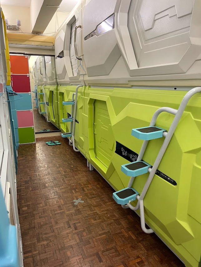 Guest relaxing inside a capsule pod with personal climate control at Pelangi Hostel