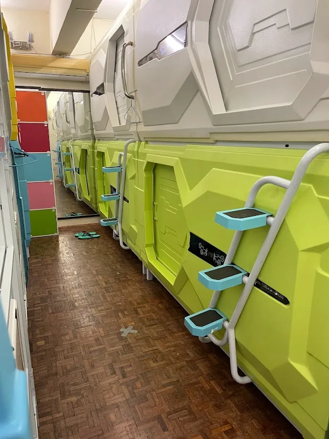 Guest relaxing inside a capsule pod with personal climate control at Pelangi Hostel
